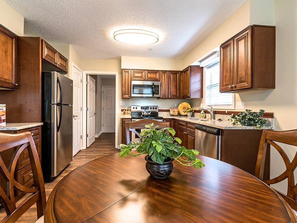 A modern kitchen with wooden cabinets, stainless steel appliances, and a dining table adorned with a potted plant.