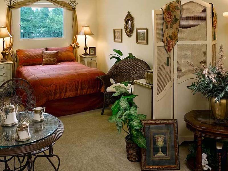 A cozy bedroom with vintage decor and warm lighting, featuring a comfortable bed, plants, and artwork.