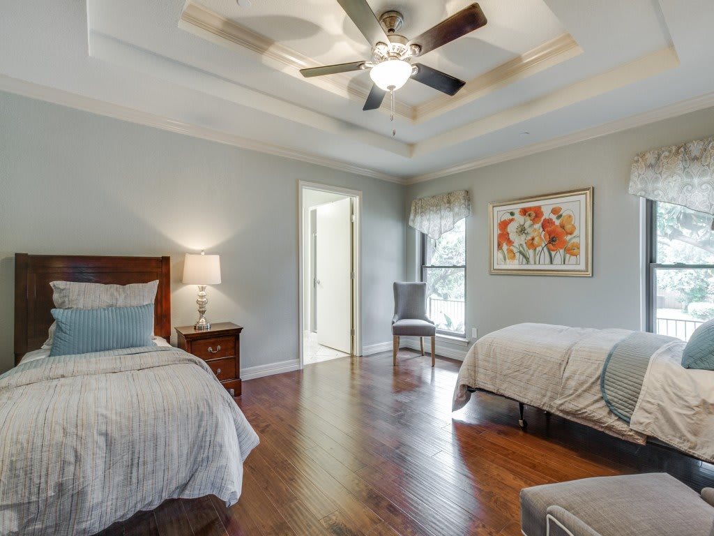 A modern bedroom featuring twin beds, wooden floors, and a ceiling fan.