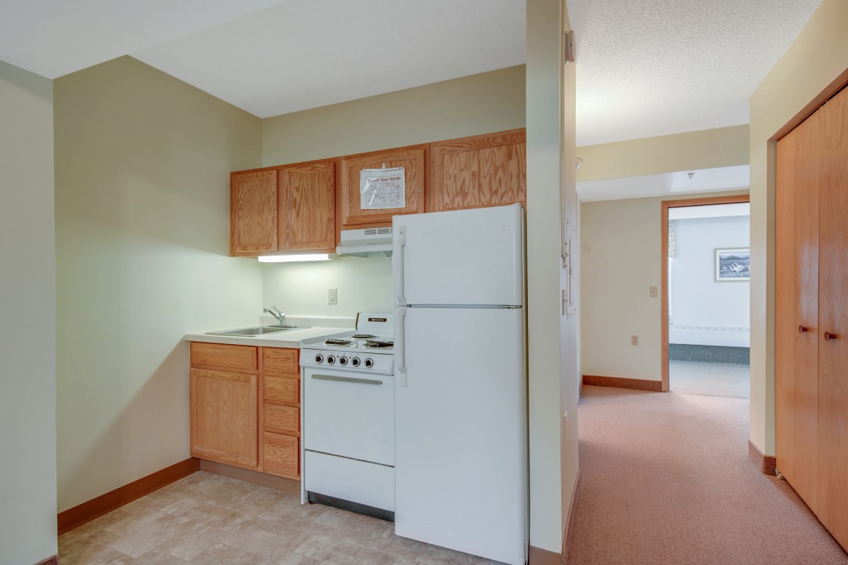 A compact kitchen area in an apartment with wooden cabinets, a refrigerator, and a stove.