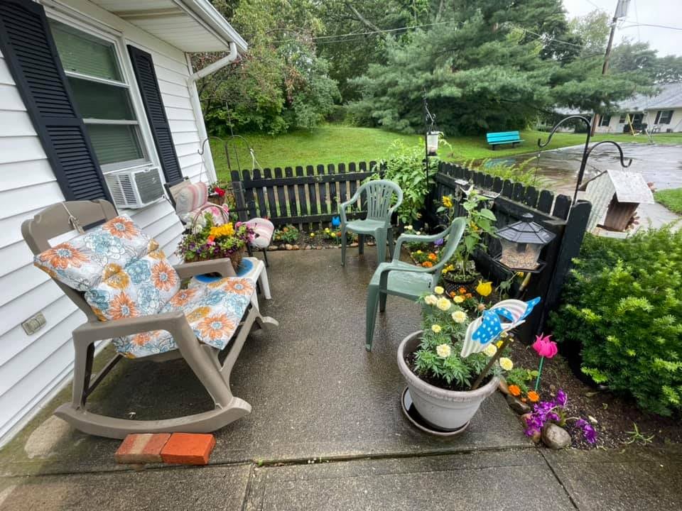 A cozy patio featuring various plants and flowers, with comfortable seating including a rocking chair.