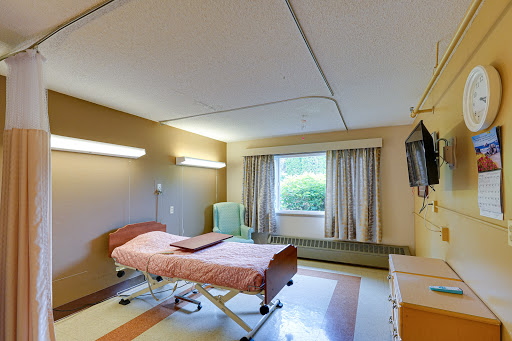 A patient room in a hospital featuring a bed, window with curtains, and basic furnishings.