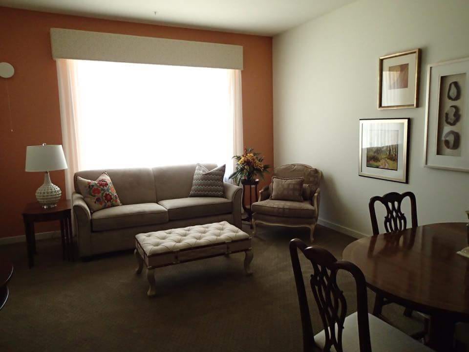 A cozy living room with a sofa, armchair, and a coffee table, featuring a dining area and wall art.