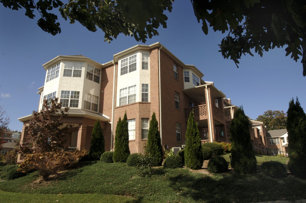 A multi-story apartment building with a brick exterior, surrounded by well-maintained landscaping and trees.