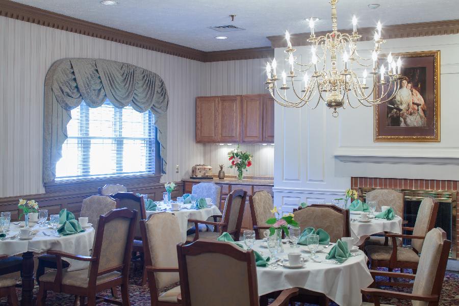 An elegant dining room with tables set for a meal, featuring a chandelier and cozy decor.
