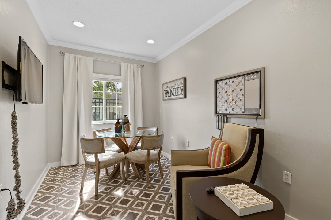 A modern dining room featuring a geometric patterned rug, a glass-top table with chairs, decorative wall art, and bright natural lighting.