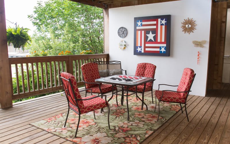 An inviting outdoor patio with a table and red cushioned chairs, accented by patriotic artwork on the wall.