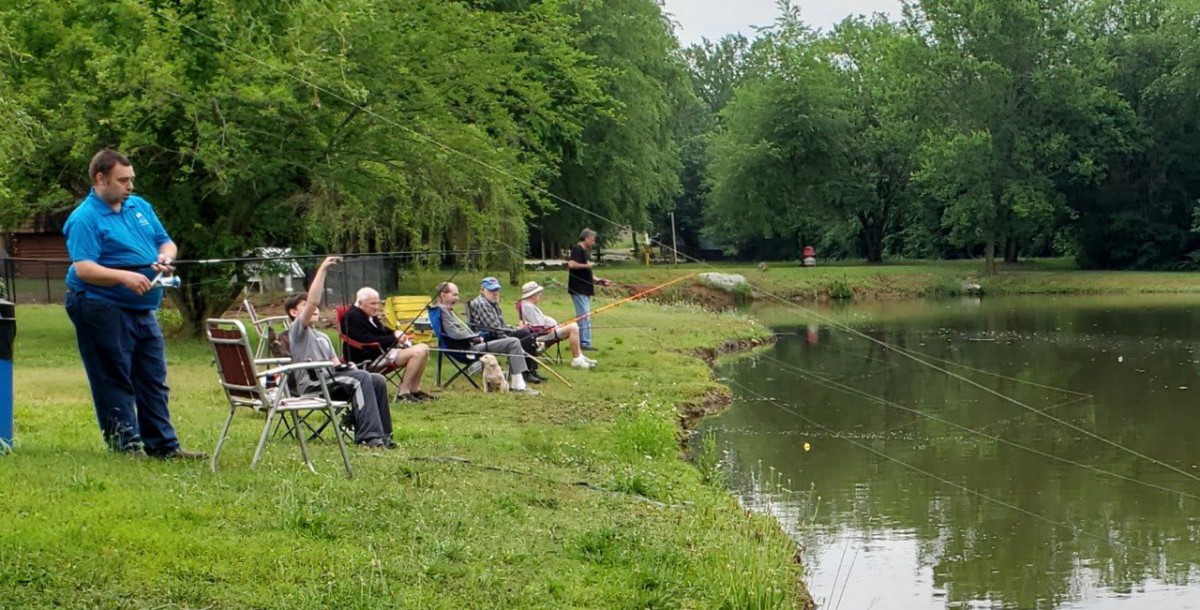 A group of people fishing by a tranquil lakeside surrounded by greenery.