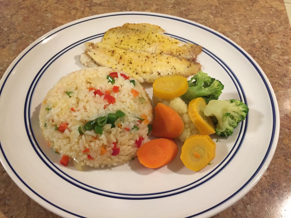 A plate of fish with rice and mixed vegetables.