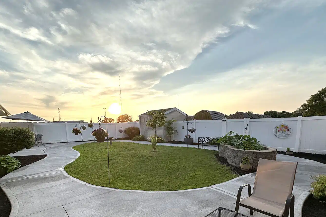 A serene backyard with a grassy lawn and a paved patio, captured at sunset.