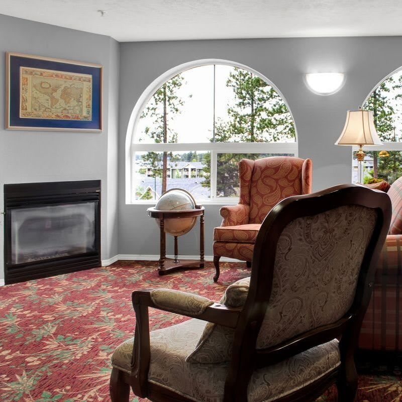A cozy living room with armchairs, a fireplace, and large windows offering a view of the outdoors.