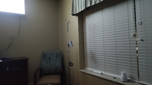 A tranquil hospital room featuring a patient chair and an intravenous pole beside a window with blinds.