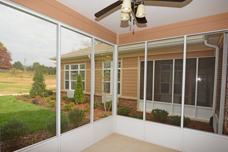 A sunroom with large windows overlooking a garden, equipped with a ceiling fan.