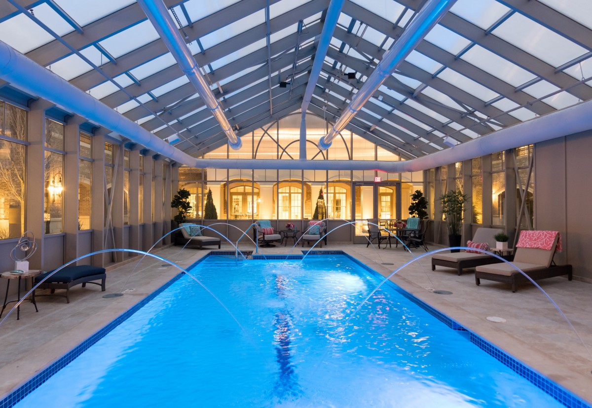 A luxurious indoor swimming pool with a glass ceiling and comfortable lounging area.
