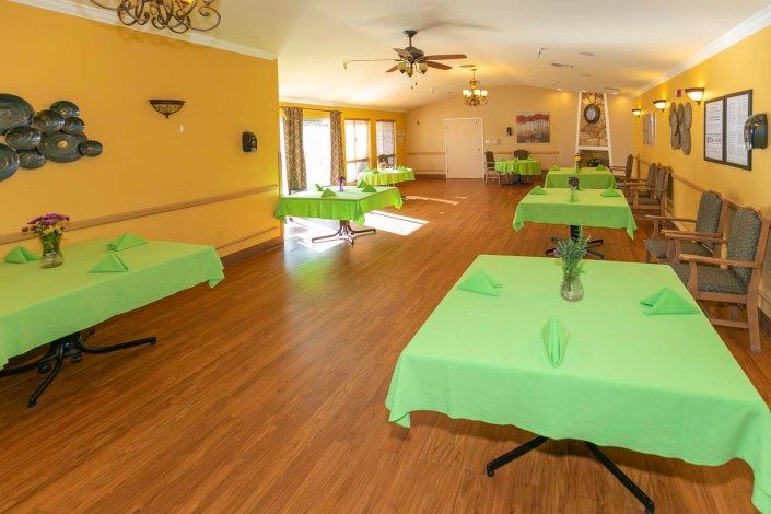 A spacious dining room with green tablecloths and wooden flooring.