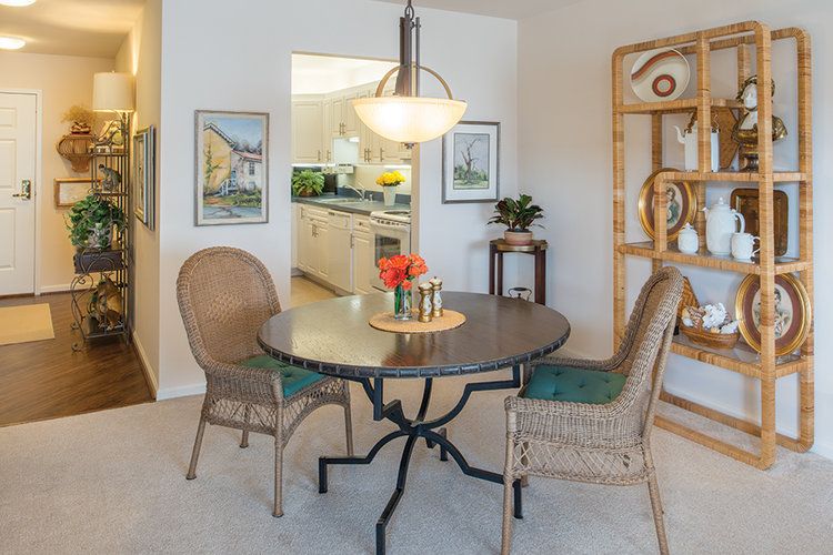 A cozy dining area with a round table and wicker chairs, featuring a decorative centerpiece and an open view into the kitchen.
