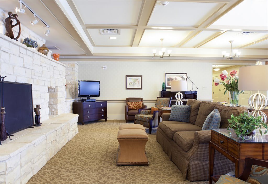 A cozy living room with a sofa, armchairs, and a television, featuring a stone fireplace and carpeted flooring.