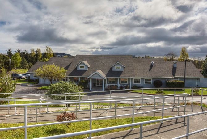 A nursing home building with accessible ramps and surrounding greenery under a cloudy sky.