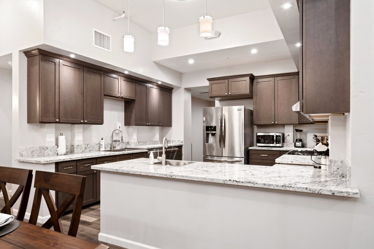 A modern kitchen featuring stainless steel appliances, white countertops, and dark wood cabinets.