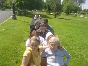A group of people sitting in a line on the grass in a park on a sunny day.