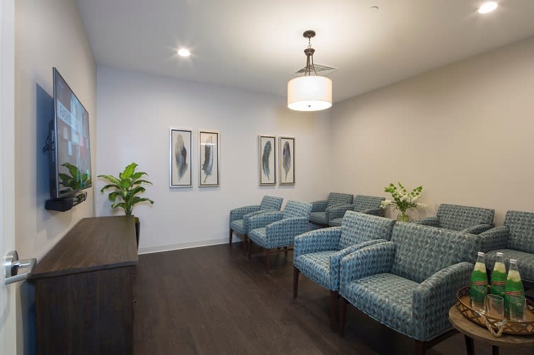 A cozy waiting room featuring blue patterned chairs, decorative artwork, and potted plants.