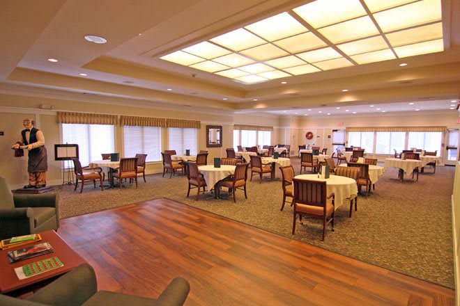 An empty dining room with tables and chairs arranged neatly, featuring both carpeted and wooden flooring.