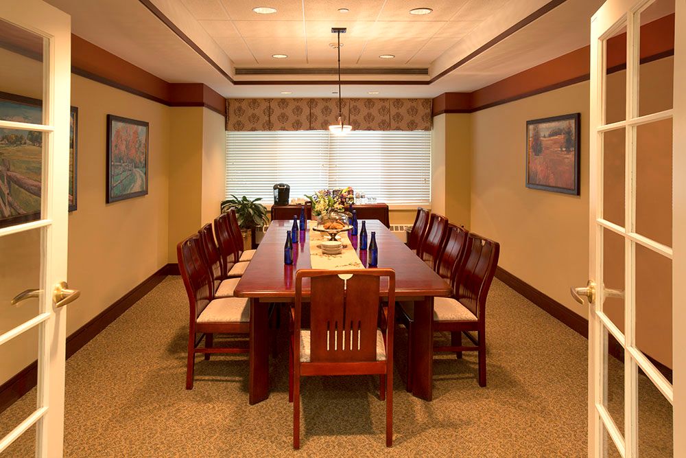 A well-furnished dining room with a long wooden table and chairs, decorated with art and lit by a hanging light fixture.
