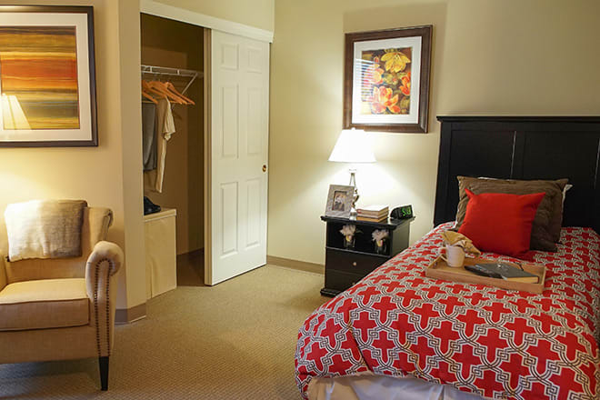 A cozy bedroom featuring a neatly made bed, a bedside table with a lamp, and an open closet.