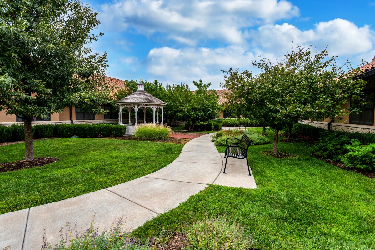 A serene garden with a curved pathway leading to a gazebo, surrounded by lush greenery and trees.