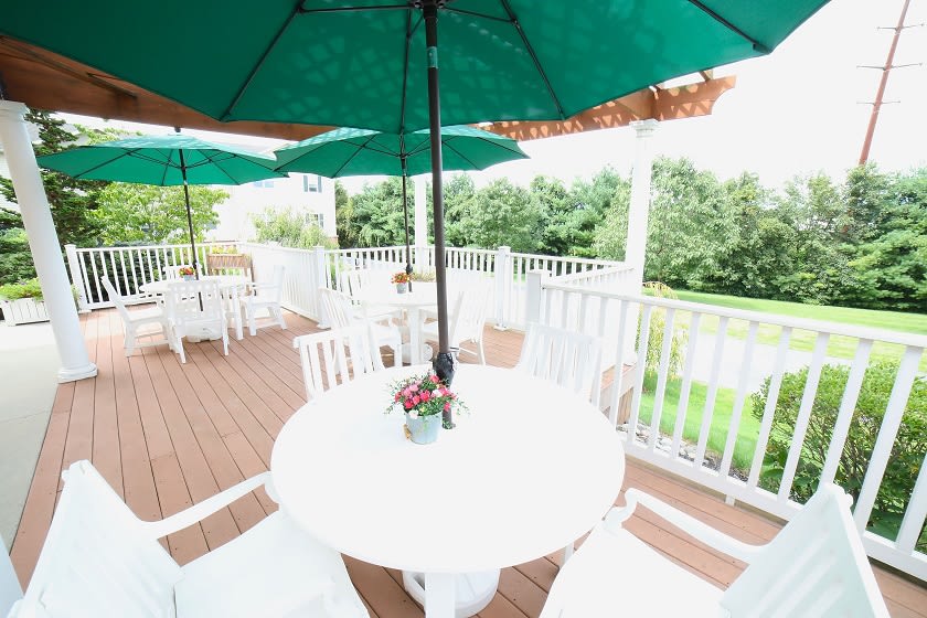 A serene outdoor patio with white furniture and green umbrellas overlooking a lush garden.