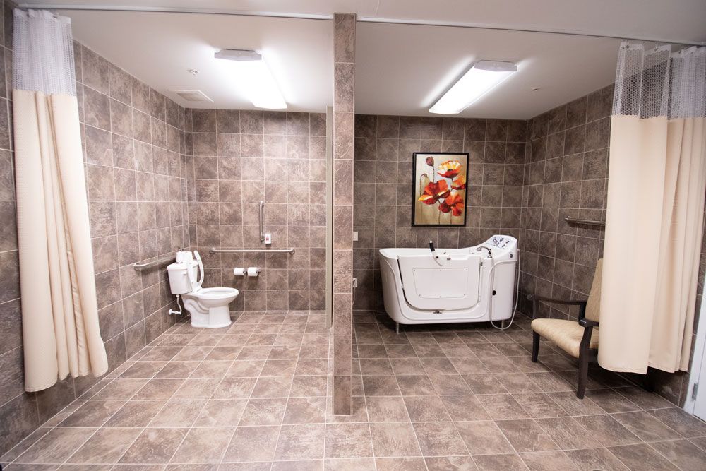 A spacious, accessible bathroom featuring a bathtub with a door and a toilet with grab bars, all set against a tiled backdrop.