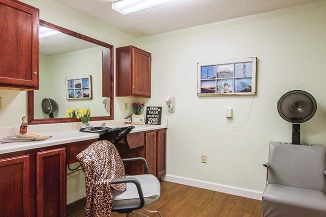 A neatly organized salon interior with a mirror, chair, and wooden cabinets.