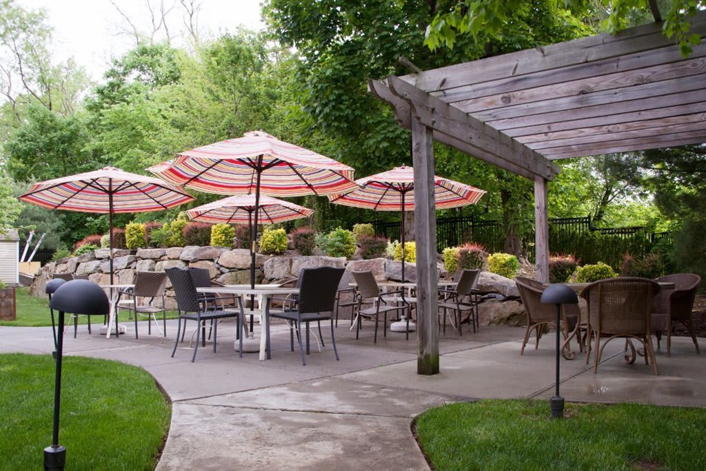 An inviting outdoor patio space with seating, umbrellas, and a pergola surrounded by greenery.