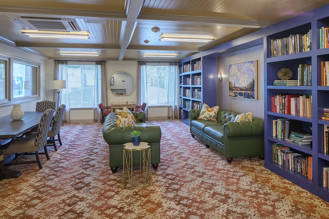 A cozy library room with green sofas, bookshelves, and patterned carpet.