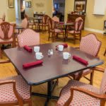 A cozy dining room setup with a square table, red napkins, and patterned chairs.
