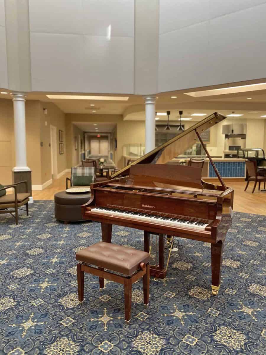 A grand piano in a spacious lobby with seating and columned architecture.