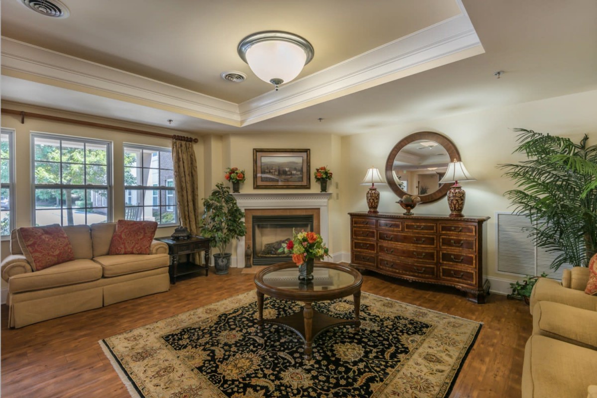 A traditional living room with classic furnishings and a fireplace, featuring a patterned rug and elegant lighting.