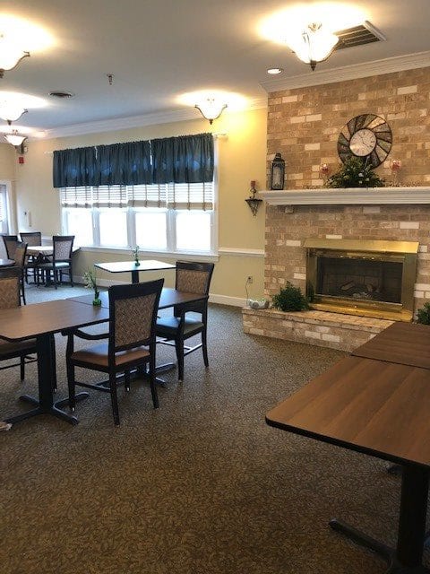 A cozy dining area with tables and chairs, featuring a brick fireplace and large windows.