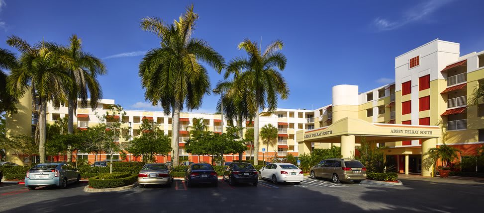 A sunny day at a hotel with palm trees and a parking lot full of cars.