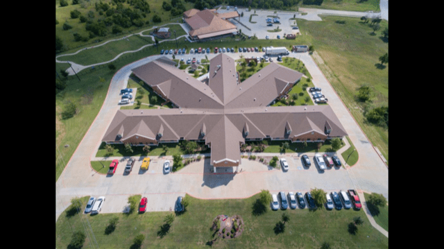 An aerial view of a uniquely designed building with a surrounding parking lot and landscaped area.