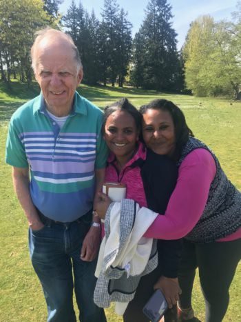 A group of three people smiling and posing together outdoors on a sunny day.