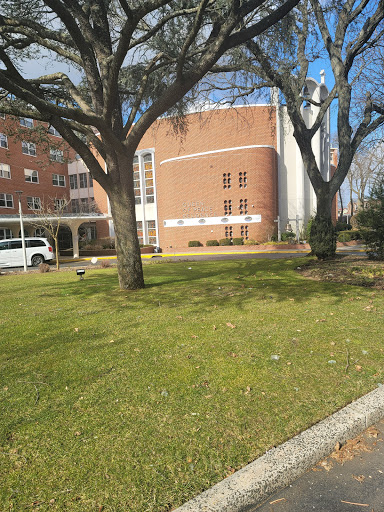 A view of a brick building surrounded by greenery and trees on a sunny day.