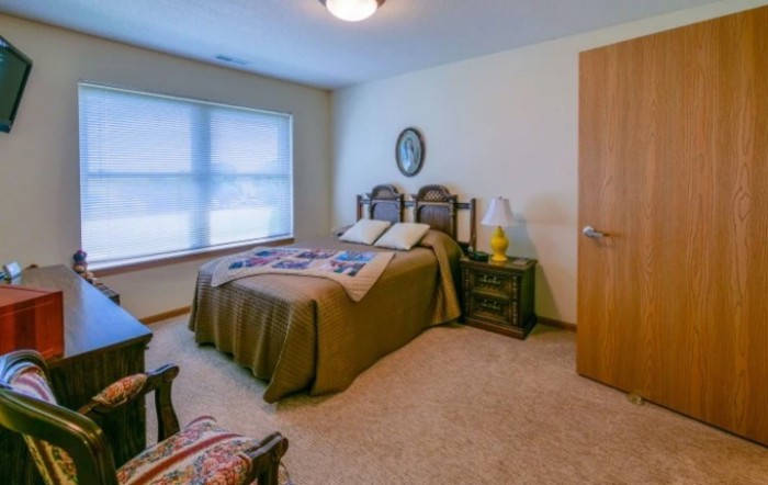 A cozy bedroom with a bed, side table, and a window letting in natural light.
