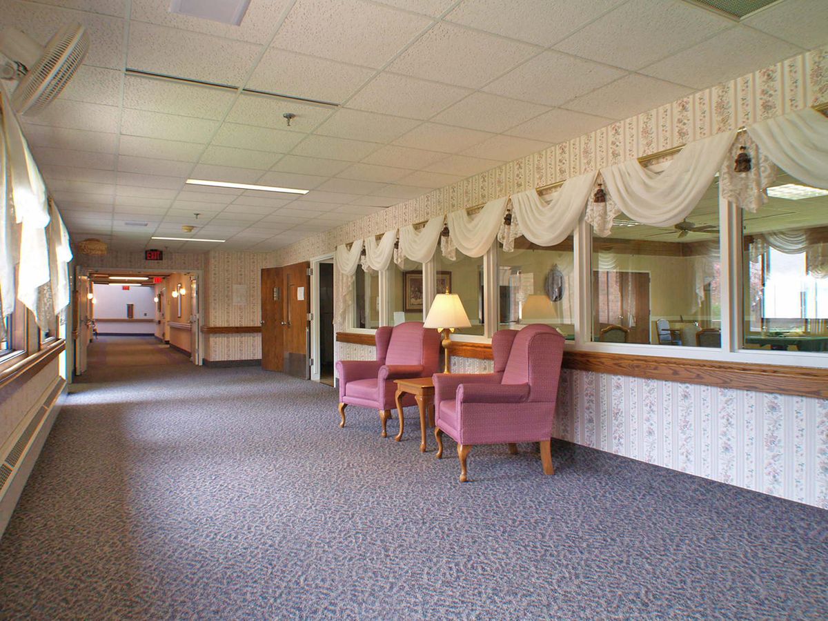 A quiet corridor with two pink armchairs and a lamp against a row of windows adorned with drapes.