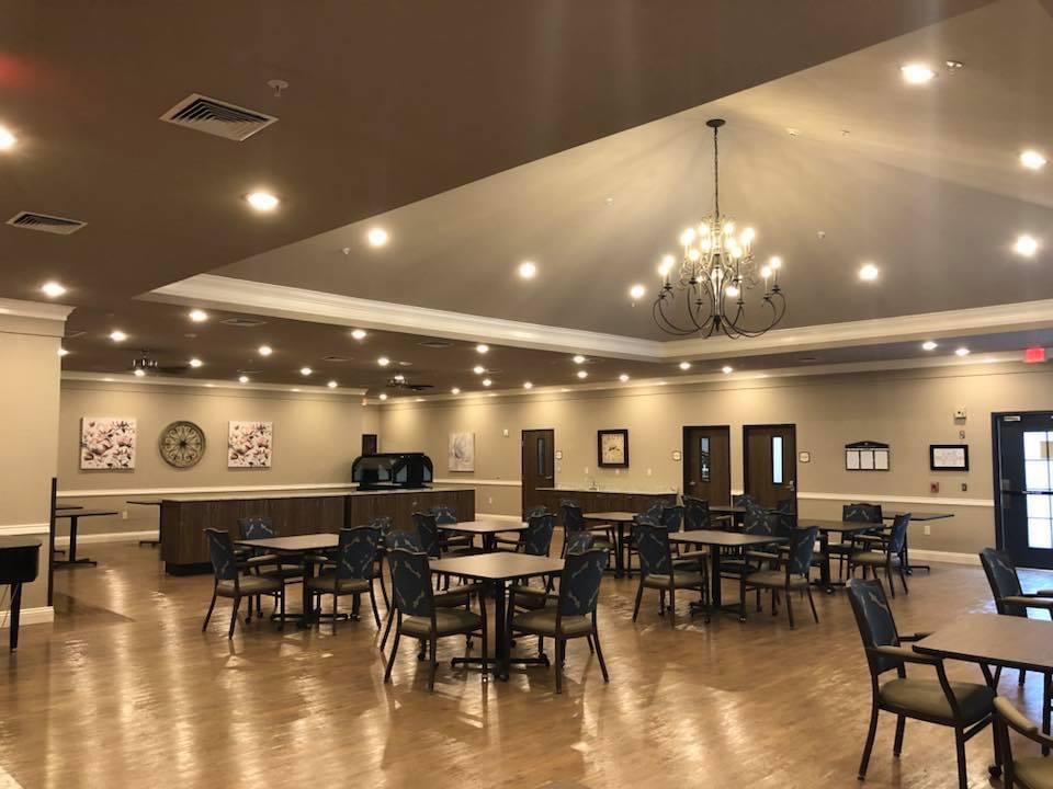 A spacious dining hall with chandeliers, wooden flooring, and neatly arranged tables and chairs.