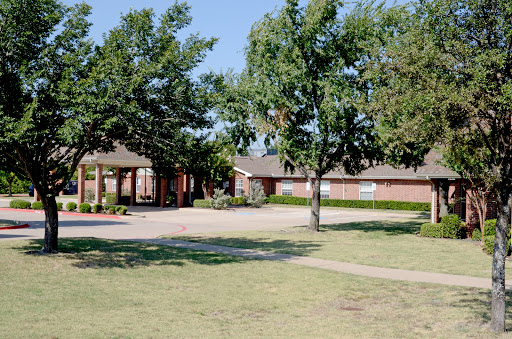 A serene view of a school surrounded by green lawns and trees under a clear blue sky.