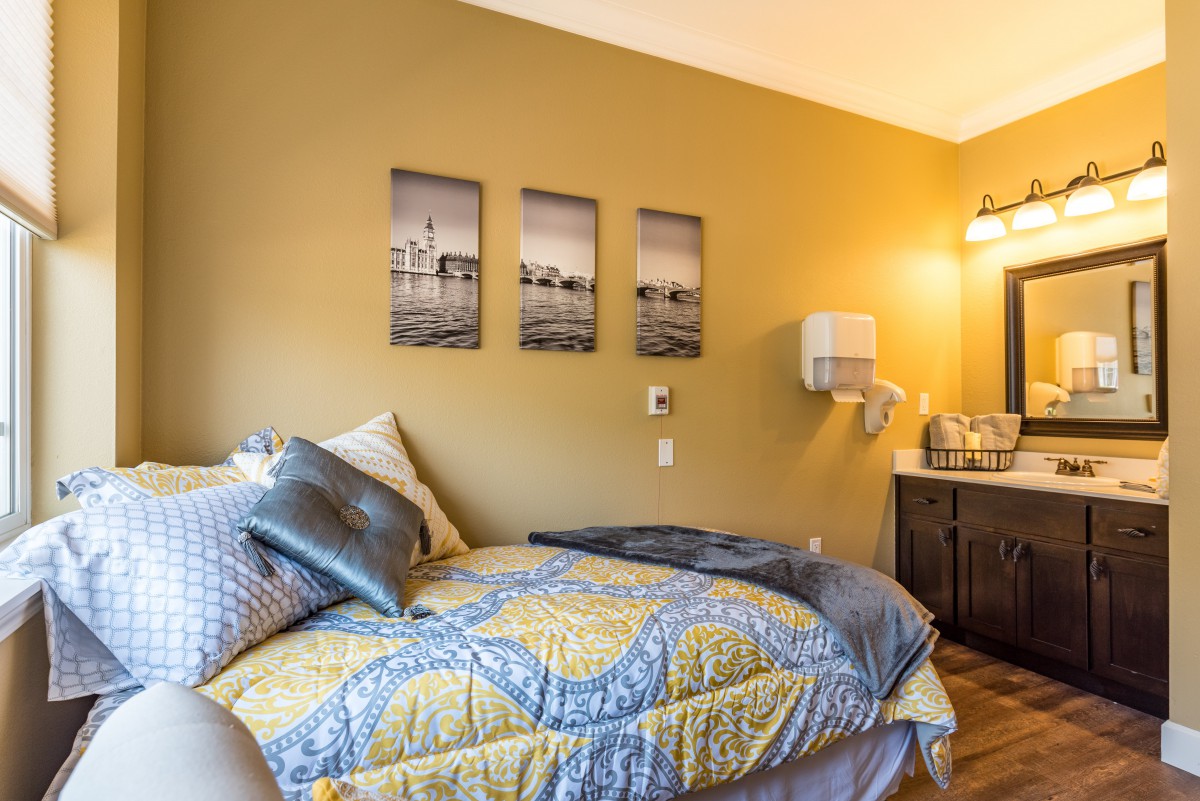 A cozy bedroom with warm lighting, featuring a bed adorned with decorative pillows and artwork on the wall.