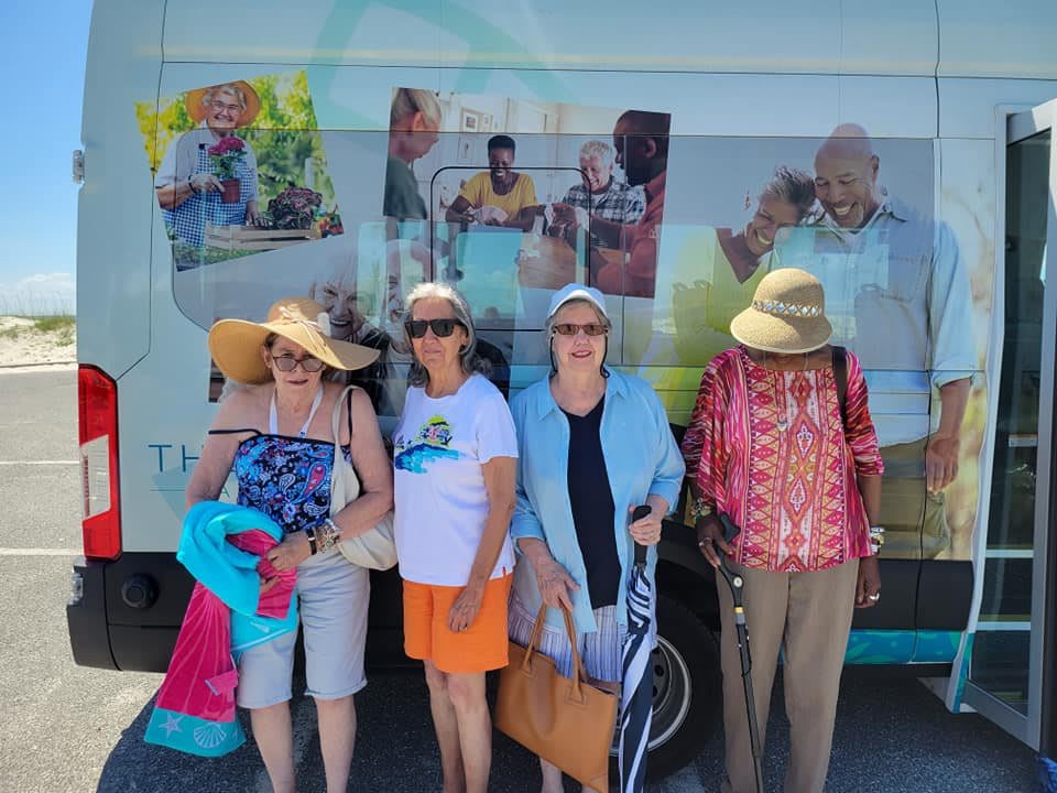 A group of seniors posing together in front of a vehicle, enjoying a sunny day out.