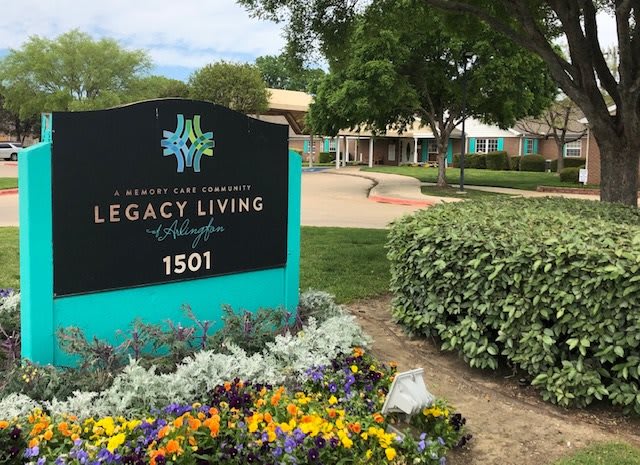 Entrance sign for Legacy Living retirement community surrounded by colorful flowers.
