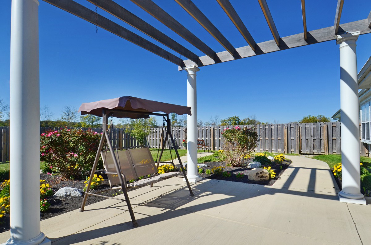 A sunny backyard patio with a pergola and a swing seat, surrounded by a garden.